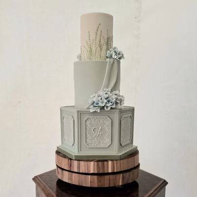 Soft sage green weding cake with a hexagonal lower tier drpaed fondant pastel blue hydrangea flowers and stencilled floral decoration